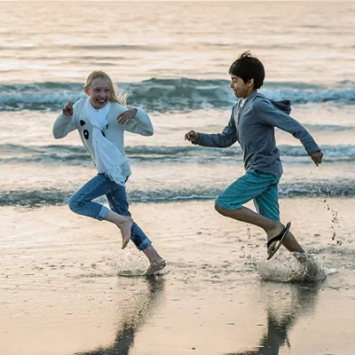 Two kids running actively and energetically on a beach alongside water